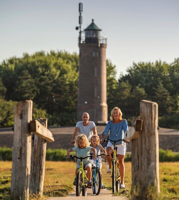 Familie beim Fahrradfahren mit dem Böhler Leuchtturm im Hintergrund