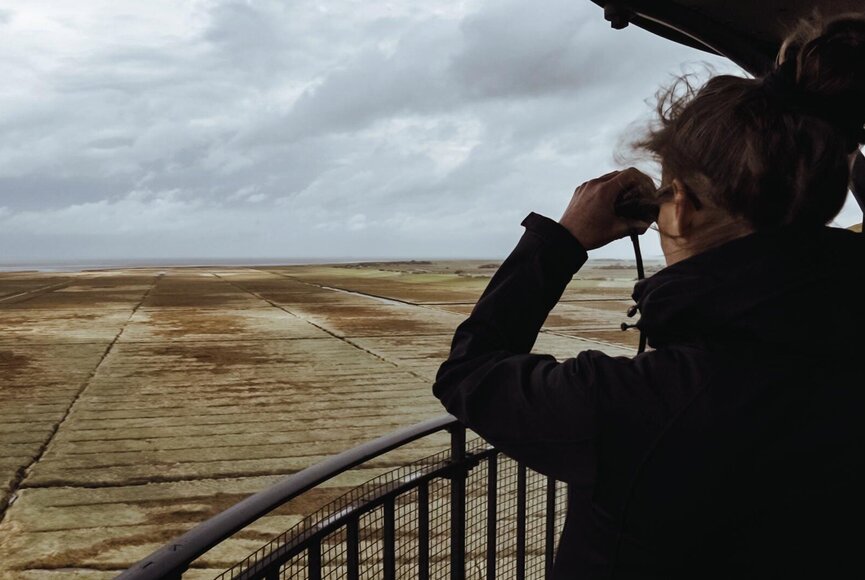 Frau schaut mit Fernglas vom Westerhever Leuchtturm über die weite Landschaft