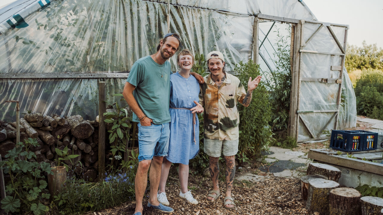 The three people from the podcast are standing in front of the greenhouse