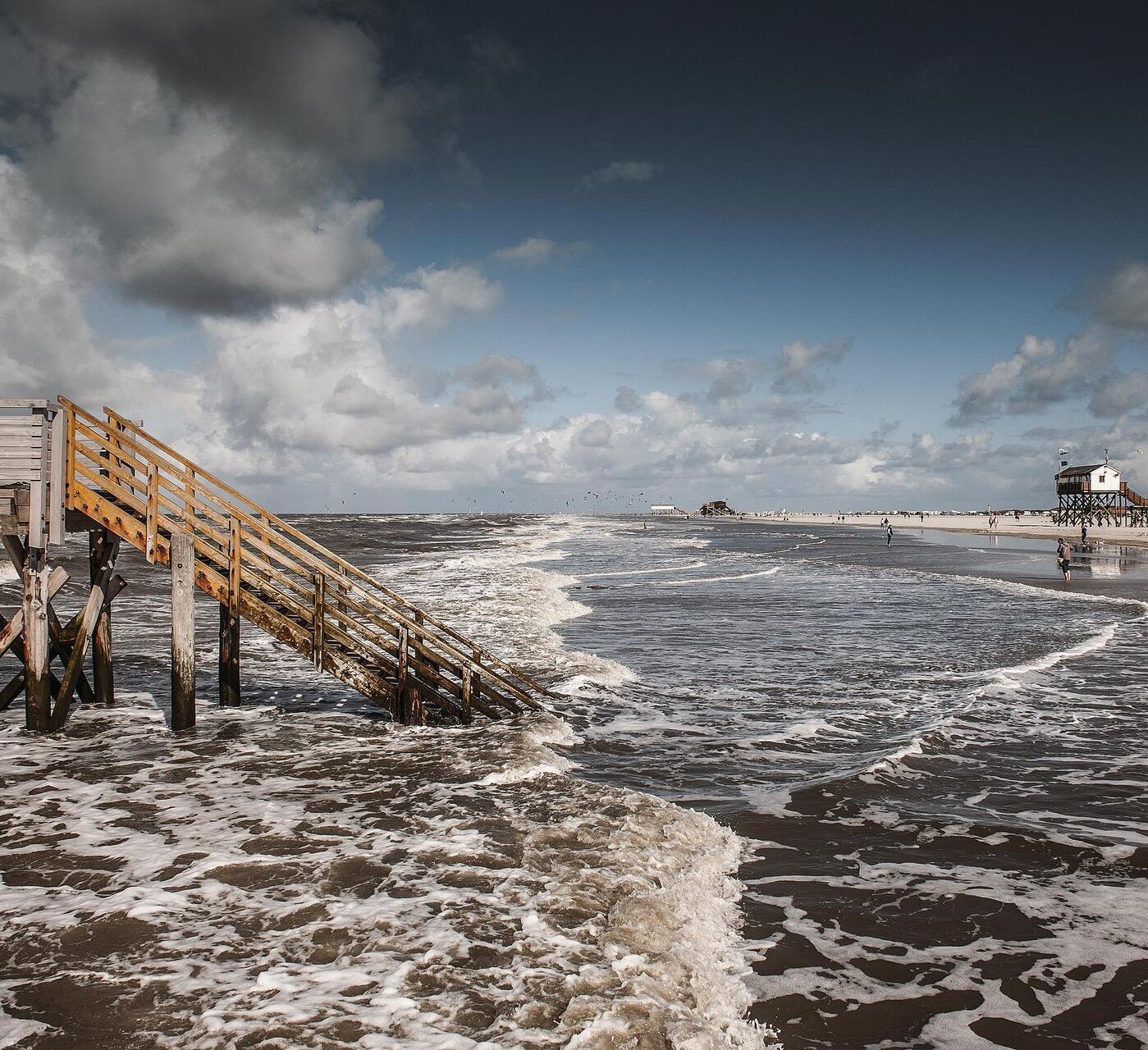 Pfahlbauten am weiten Sandstrand mit auflaufendem Wasser