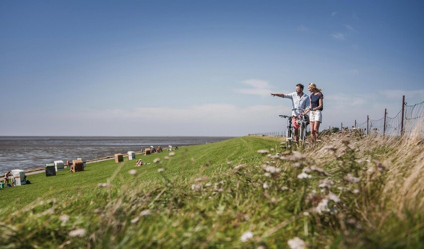 Paar schiebt Fahrräder über den grünen Deich in Vollerwiek mit Blick auf die Nordsee