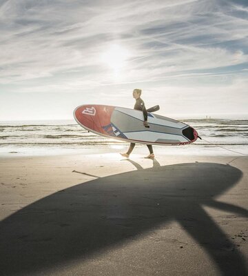 junge Dame mit Neoprenanzug und SUP-Board unter dem Arm