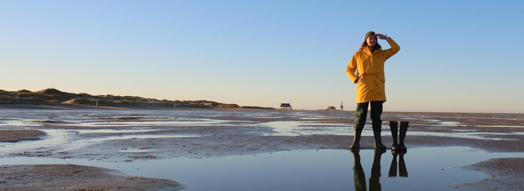 junger Mann mit gelbem Friesennerz und Gummistiefeln am Strand