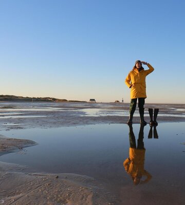 Nordfriese in gelber Regenjacke und Gumistiefeln am Strand