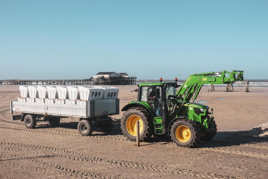 Trecker auf dem Strand mit einem Anhänger voller Strandkörbe