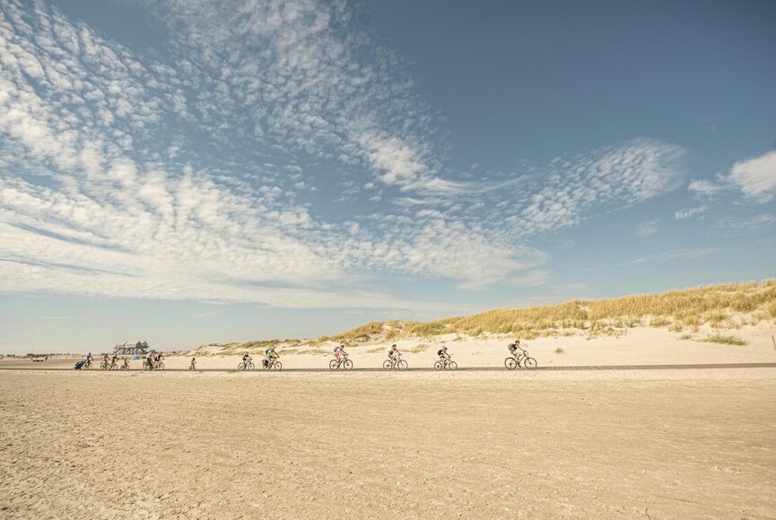 Fahrradfahrer hintereinander auf dem Holzsteg am Strand in Ording