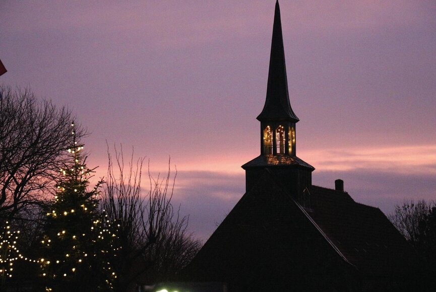 Weinachtsbeleuchtung und beleuchtete Kirchturmuhr bei Dämmerung