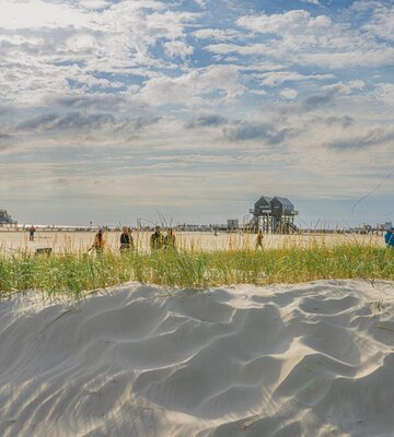 Sanddüne mit Strand, Spaziergängern und Pfahlbau im Hintergrund
