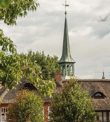 Kirchturmspitze mit niedrigeren Hausdächern davor
