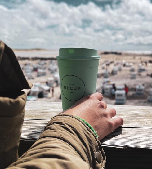 Dame hält einen RECUP Becher auf dem Mehrzweckgebäude in Ording in ihrer Hand