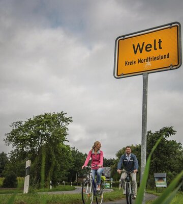Paar radelt am Ortsschild Welt vorbei