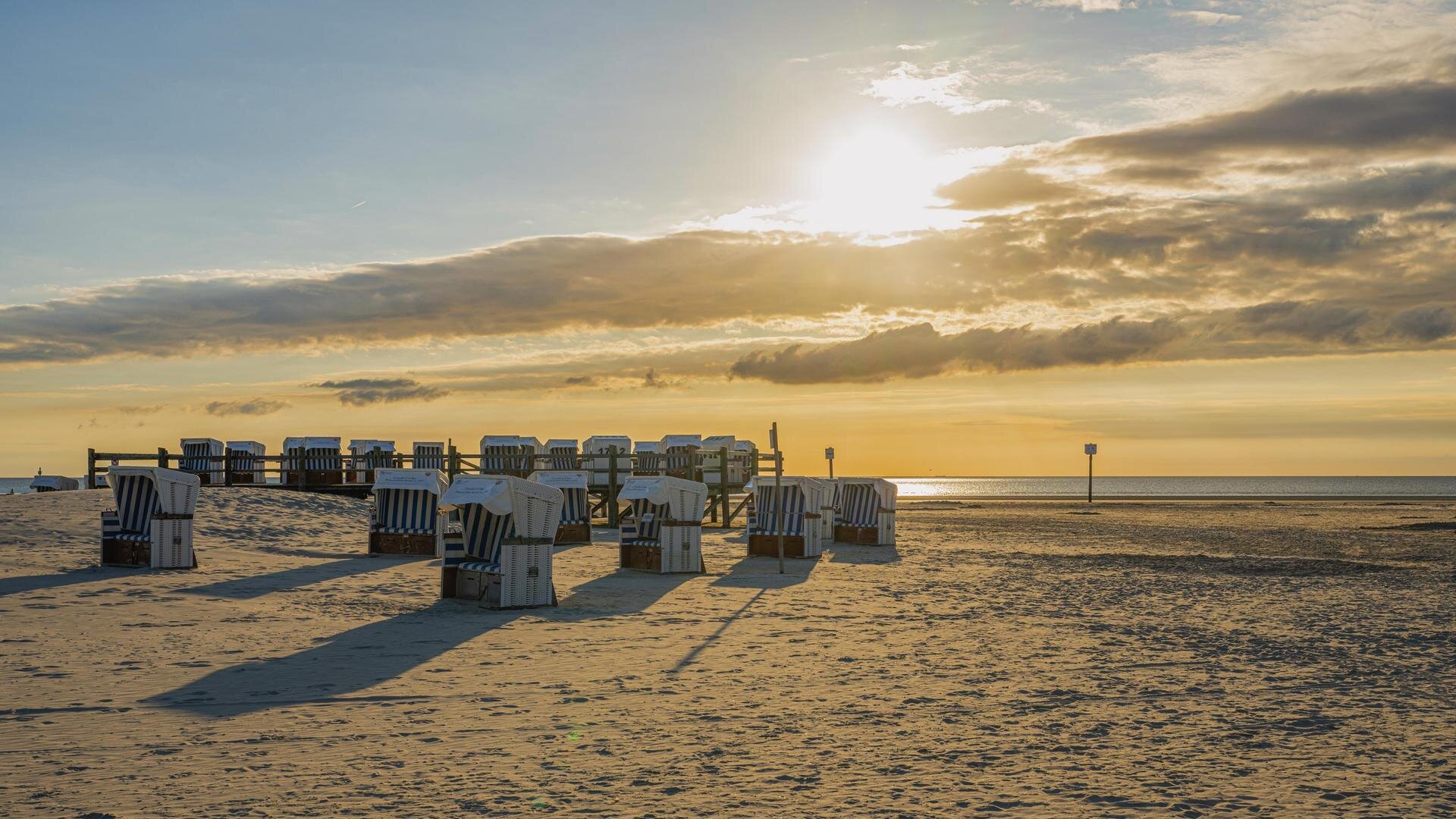 Strandkörbe im Sand und auf einem Pfahlbaupodest beim Sonnenuntergang