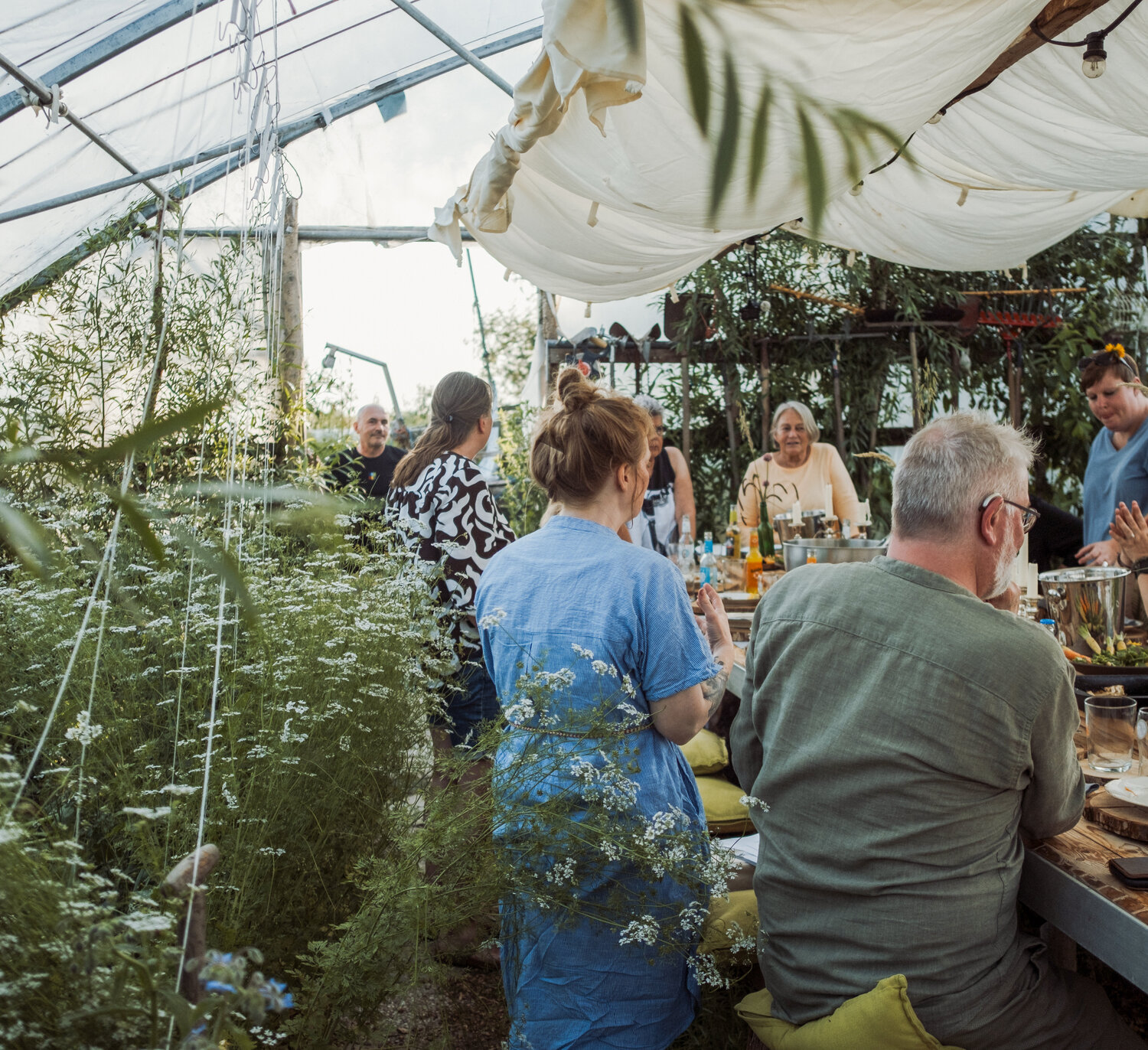 A group of people are sitting at a table in the greenhouse