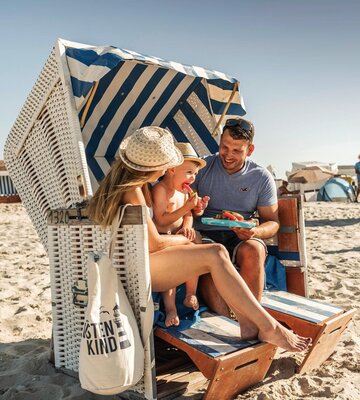 Eltern sitzen gemensam mit kleinem Sohn im Strandkorb und essen Wassermelone
