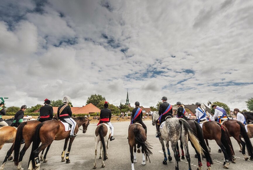 Reiter mit festlicher Kleidung und Pferden in einer Reihe auf dem Marktplatz im Dorf