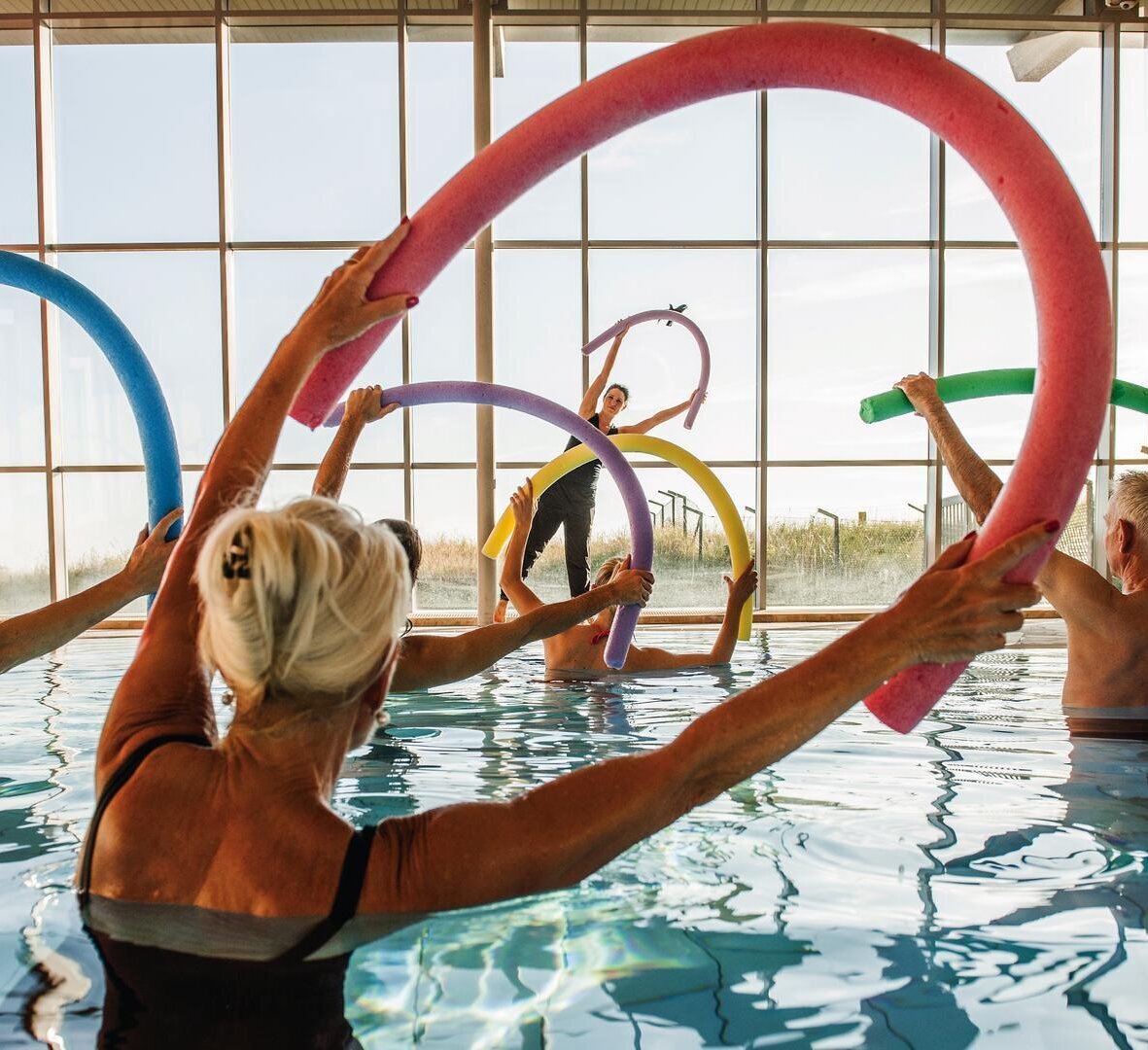 Gruppe bei Sportübungen mit Poolnudeln im Bewegungsbad