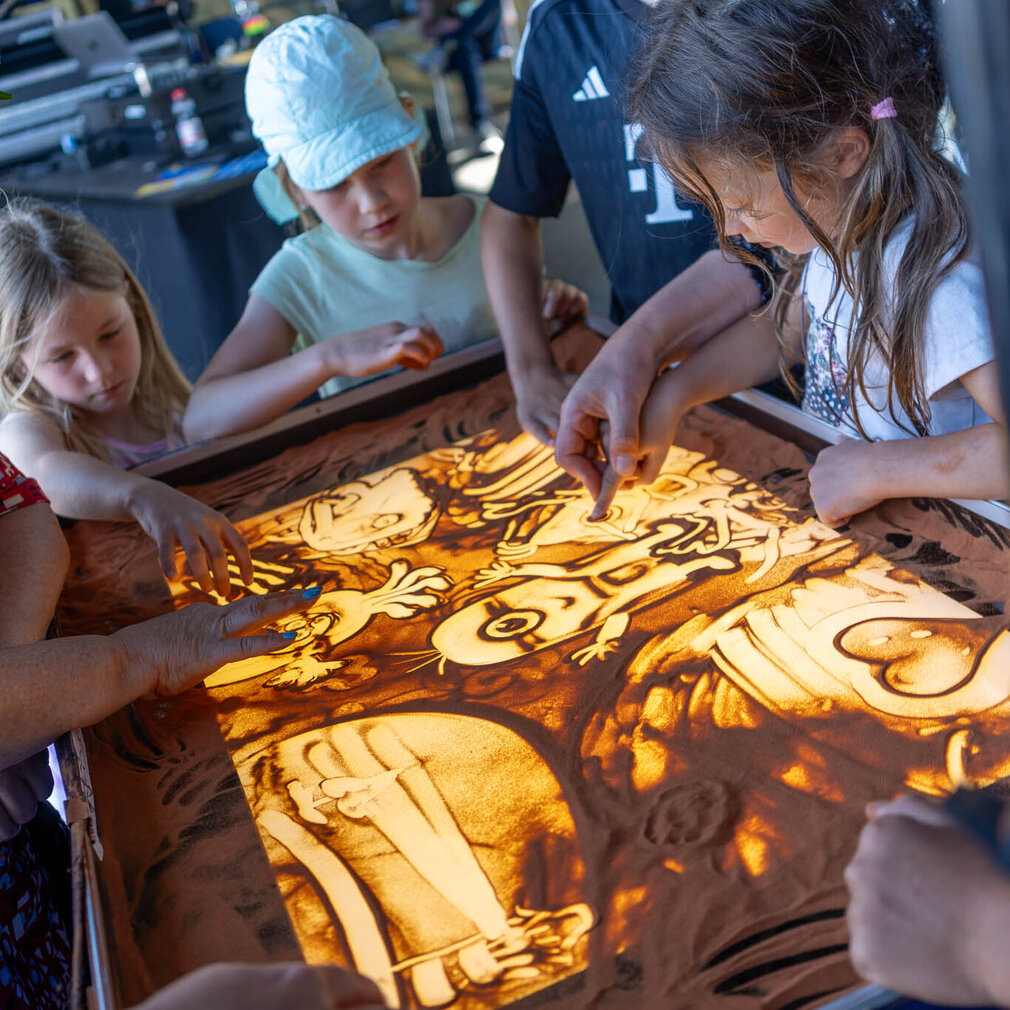 Kinder dürfen der Sandmalerin bei einem Kunstwerk helfen