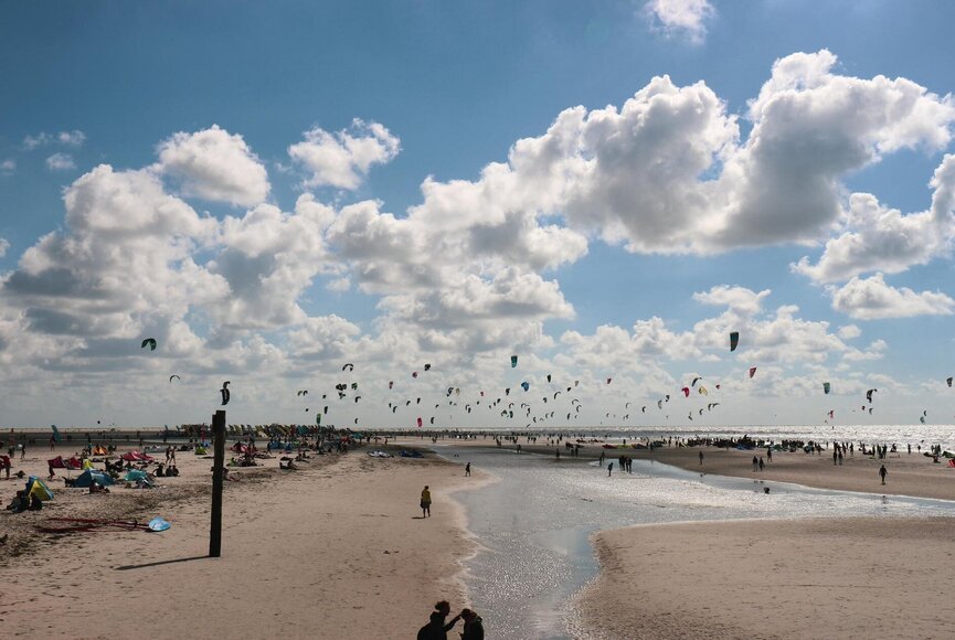 Blick über den Strand mit hunderten Kitesurfern auf dem Wasser und etlichen Zuschauern am Strand