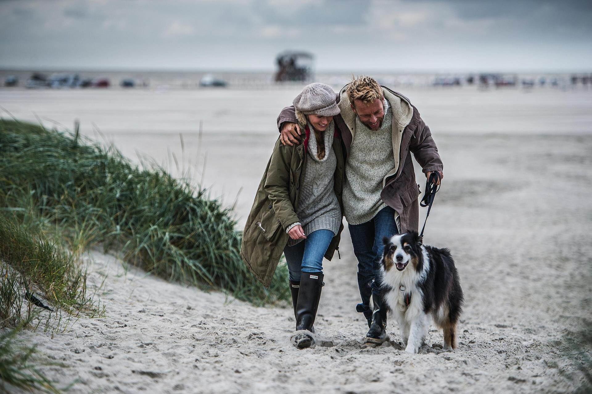 Paar mit Hund spaziert am Hundestrand