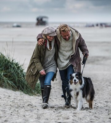 Paar mit Hund auf einem Spaziergang am Strand