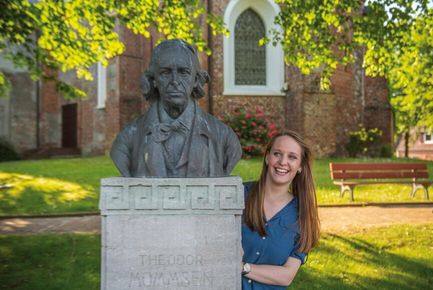 Frau schaut hinter Theodor Mommsen Denkmal hervor