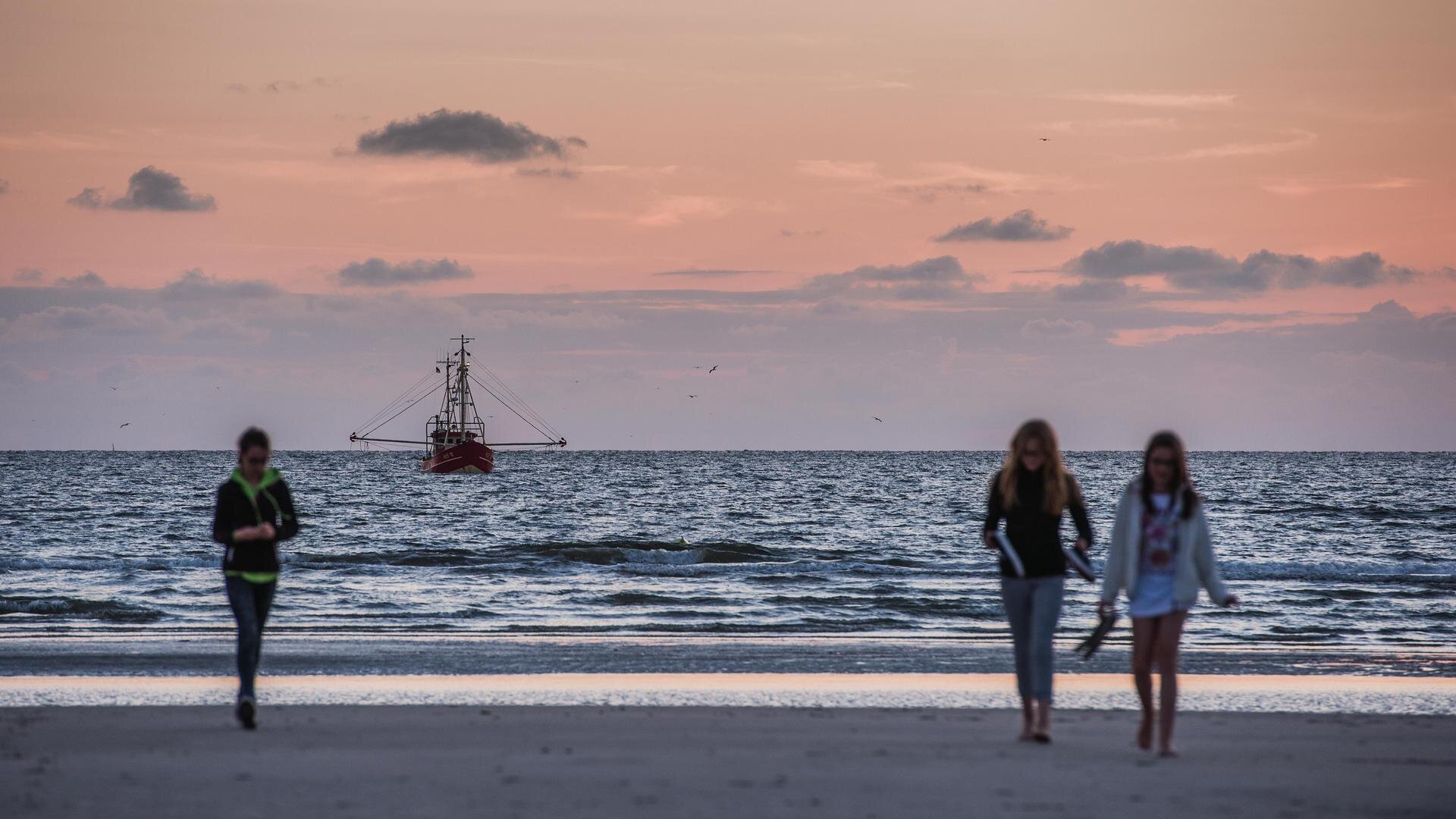 Menschen am Strand mit Kutter auf der Nordsee im Hintergrund
