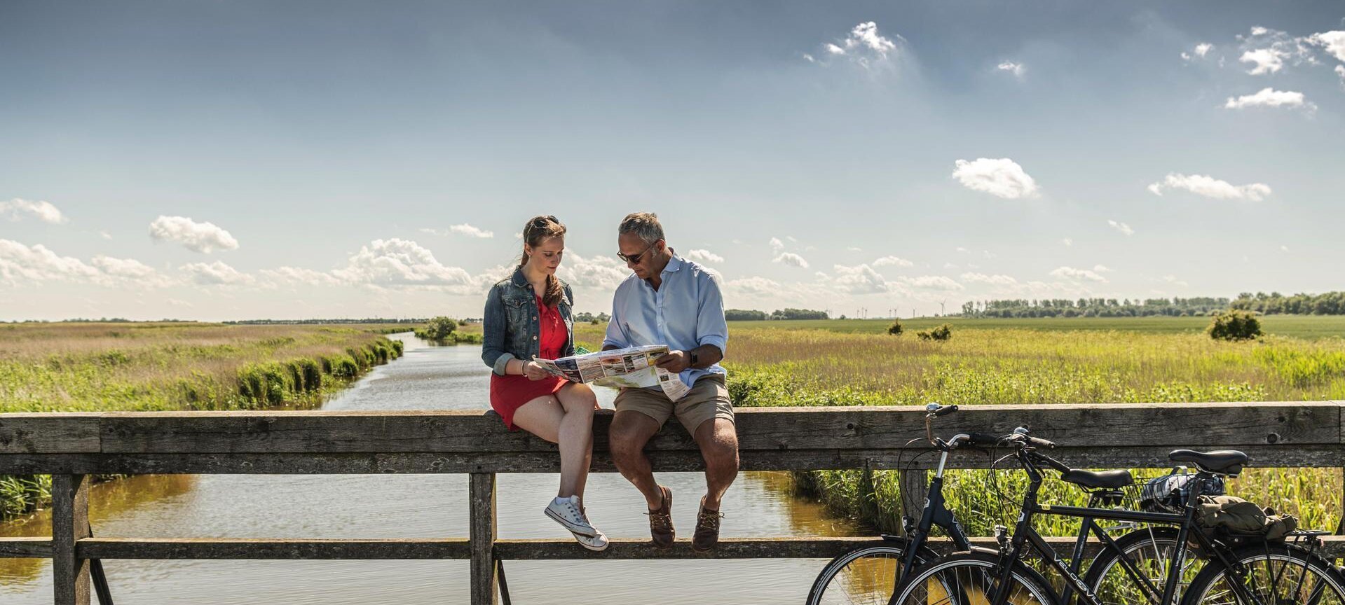 Paar sitzt auf einem Geländer in der Sonne und schaut in eine Fahrradkarte