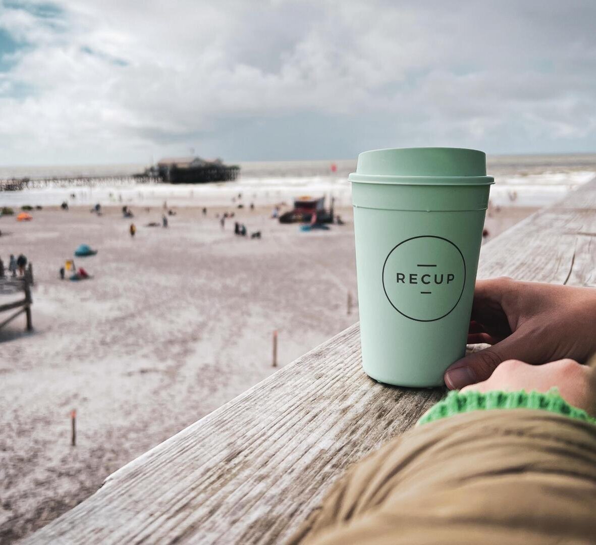 Frau mit RECUP-Bescher auf einem Pfahlbau mit Blick über den Strand