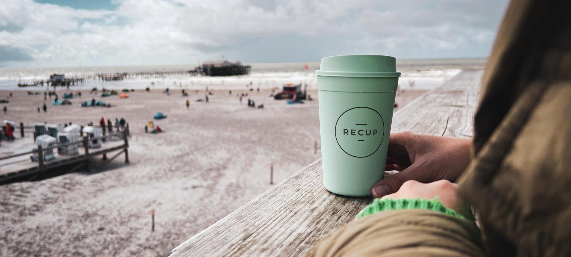 Frau mit RECUP-Bescher auf einem Pfahlbau mit Blick über den Strand