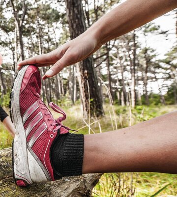 Frau beim Dehnen vor dem Joggen im Kiefernwald
