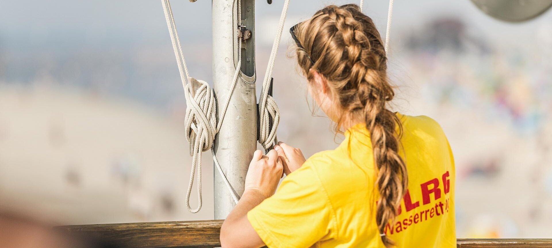 junge Mitarbeiterin der DLRG sichert die gehisste Flagge