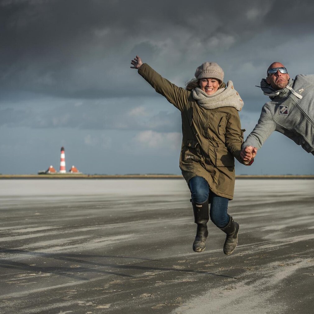 Paar springt in die Luft vor dem Westerhever Leuchtturm