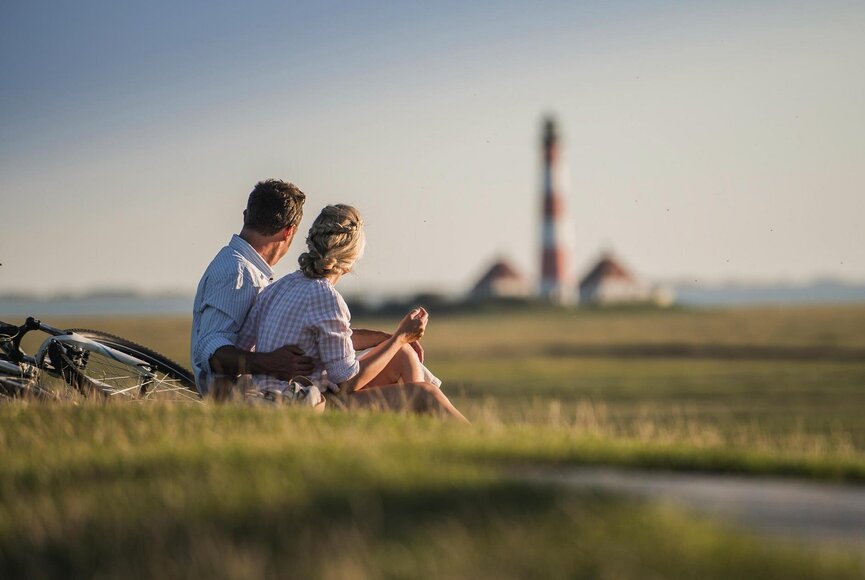 Pärchen sitzt auf dem Deich und blickt auf den Westerhever Leuchtturm