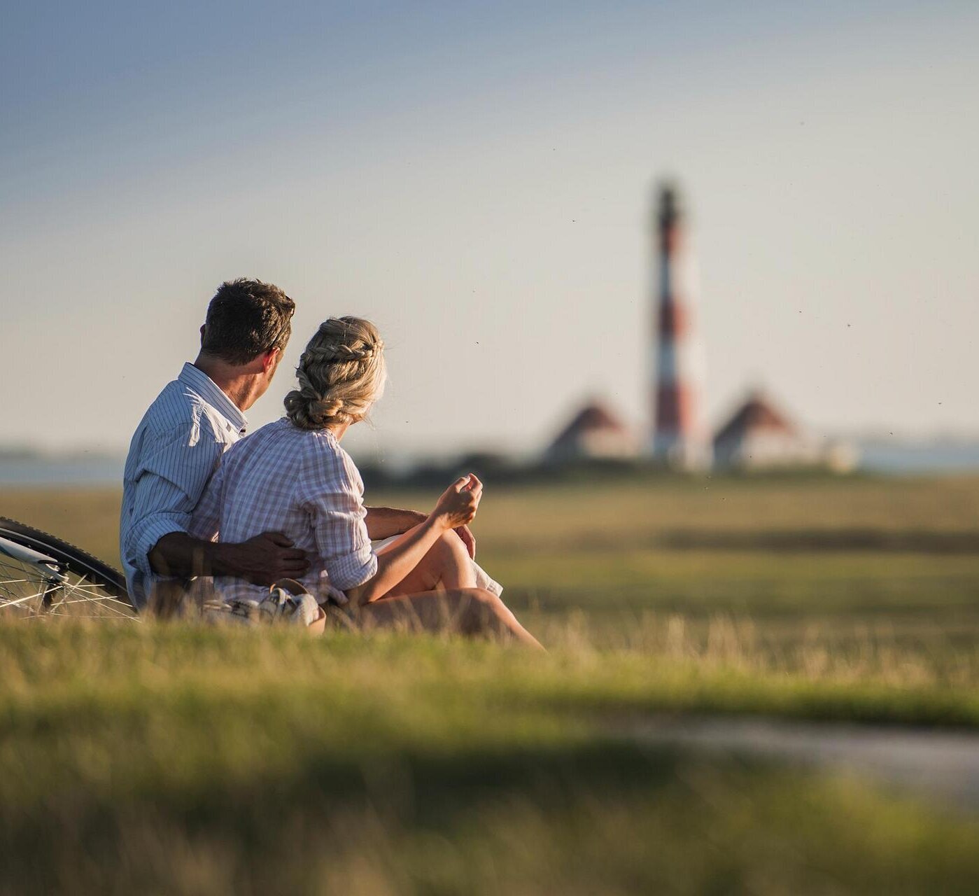 Paar sitzt auf dem Deich und blickt auf den Westerhever Leuchtturm