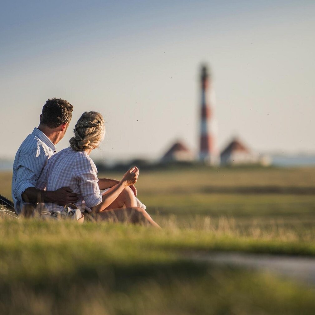 Paar sitzt auf dem Deich und blickt auf den Westerhever Leuchtturm