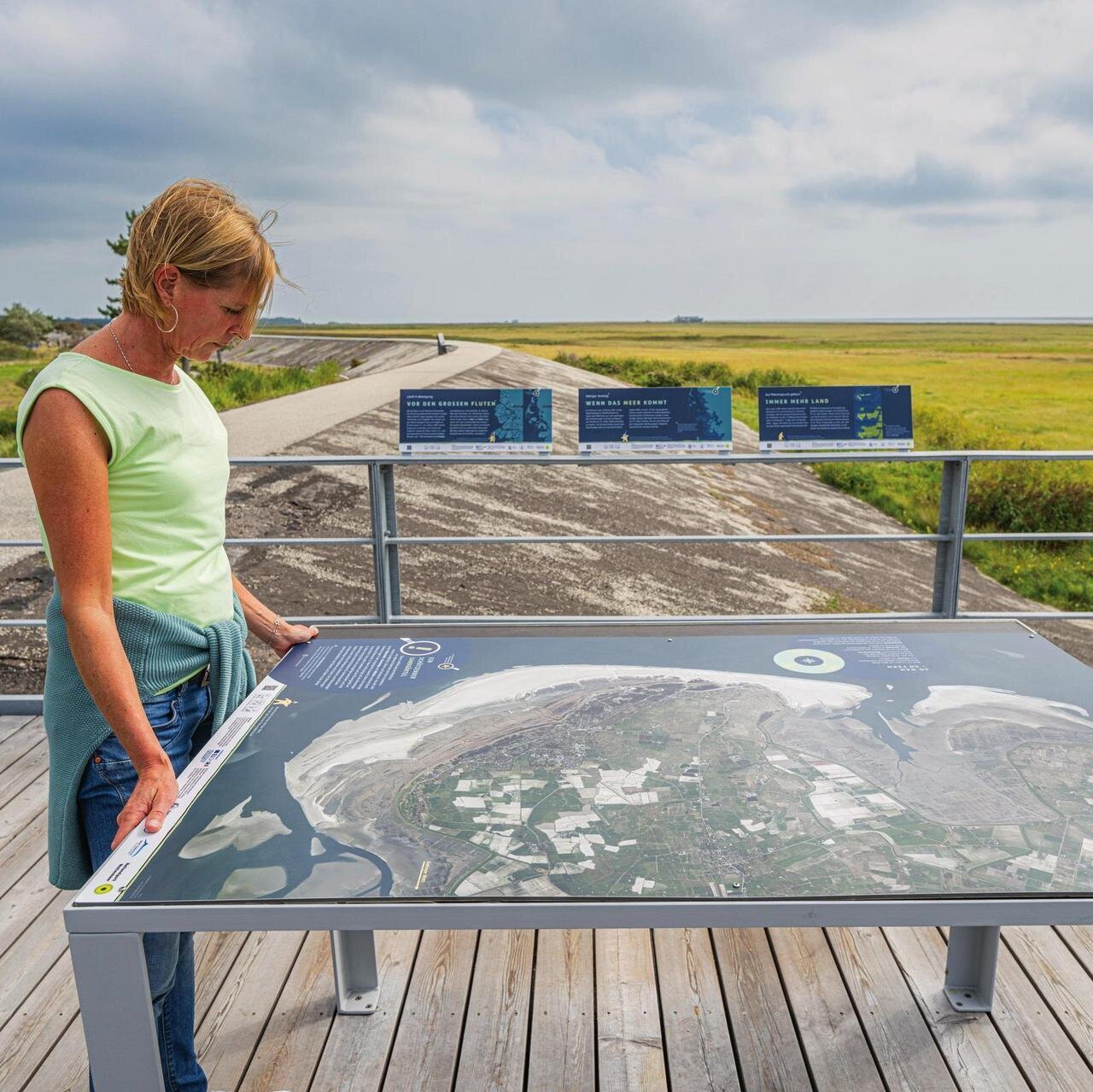Dame vor dem Schild des Weltnaturerbes Wattenmeer am Deich
