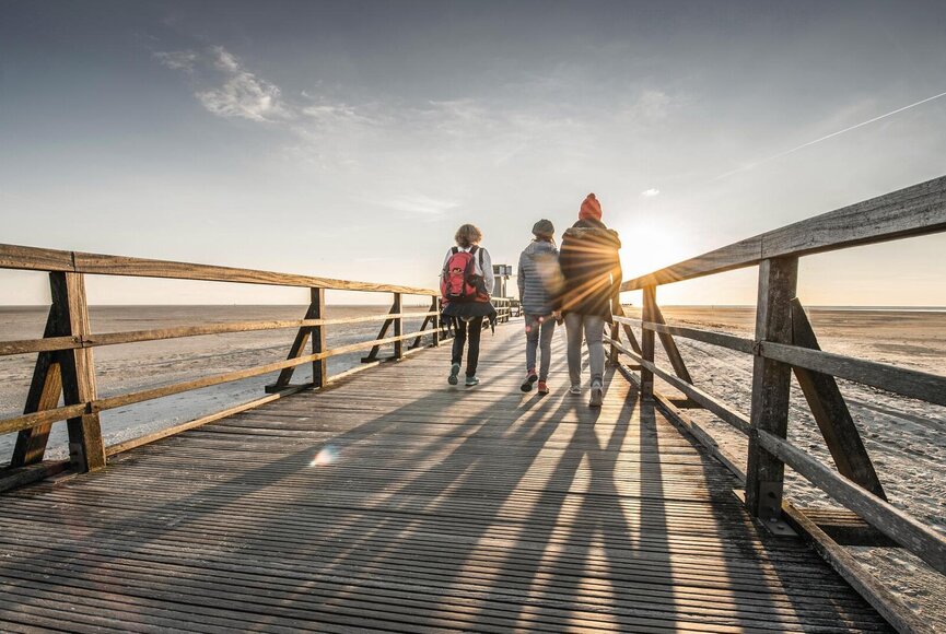 Freunde spazieren auf der Seebrücke in Richtung Nordsee bei Sonnenuntergang