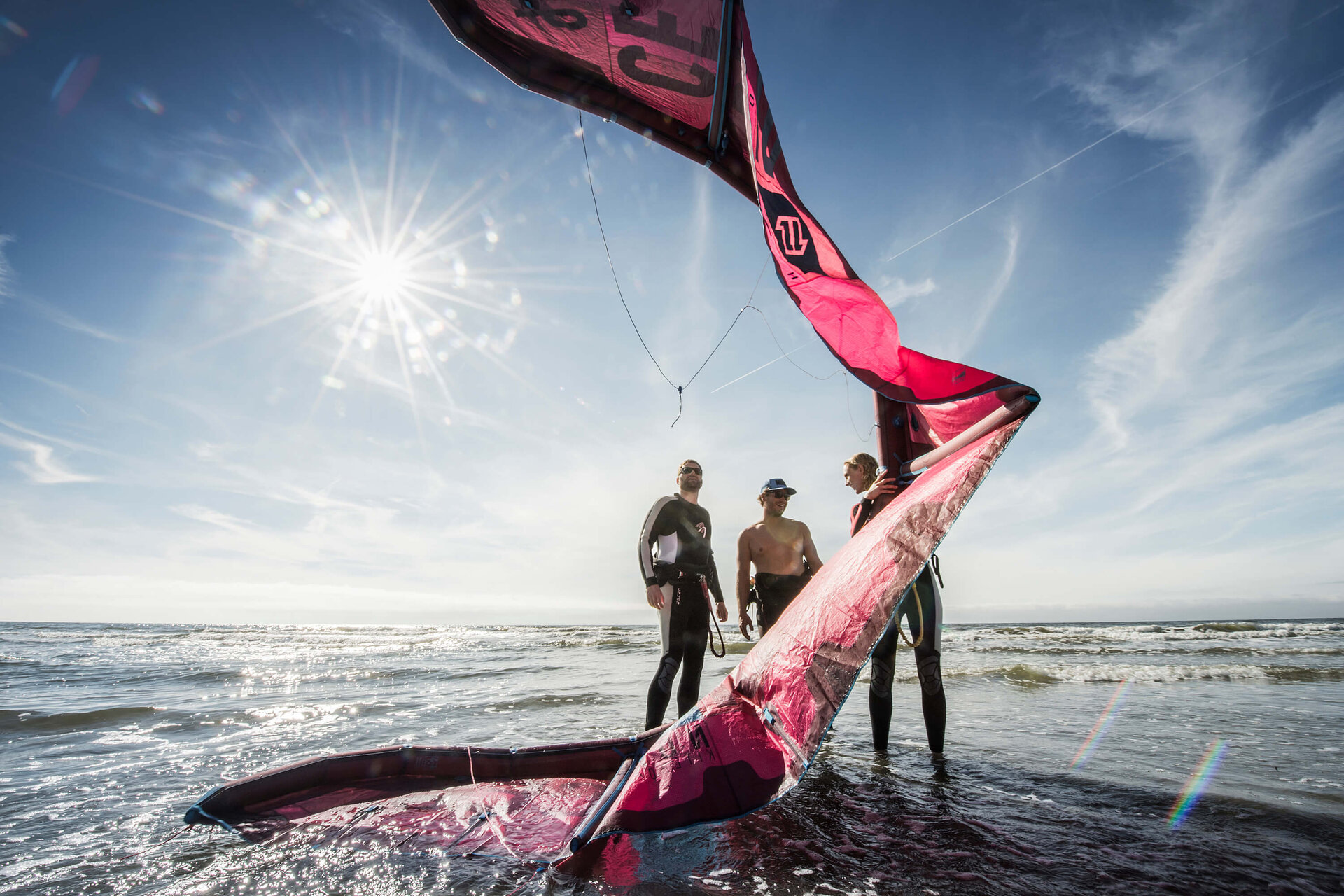 Paar mit Kitesurf-Lehrer und großer Lenkmatte am Strand