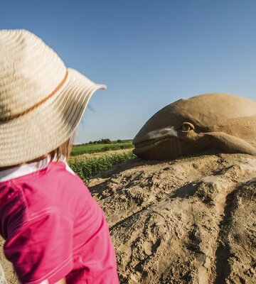 Mädchen schaut sich große Sandskulptur in Form eines Wals an