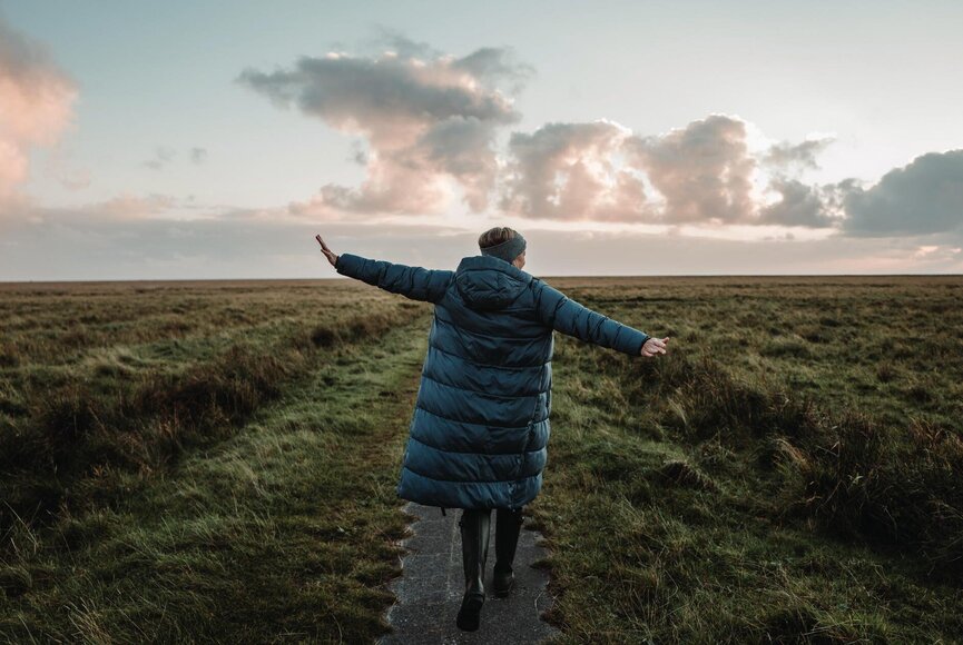 Frau mit ausgebreiteten Armen auf dem Deich
