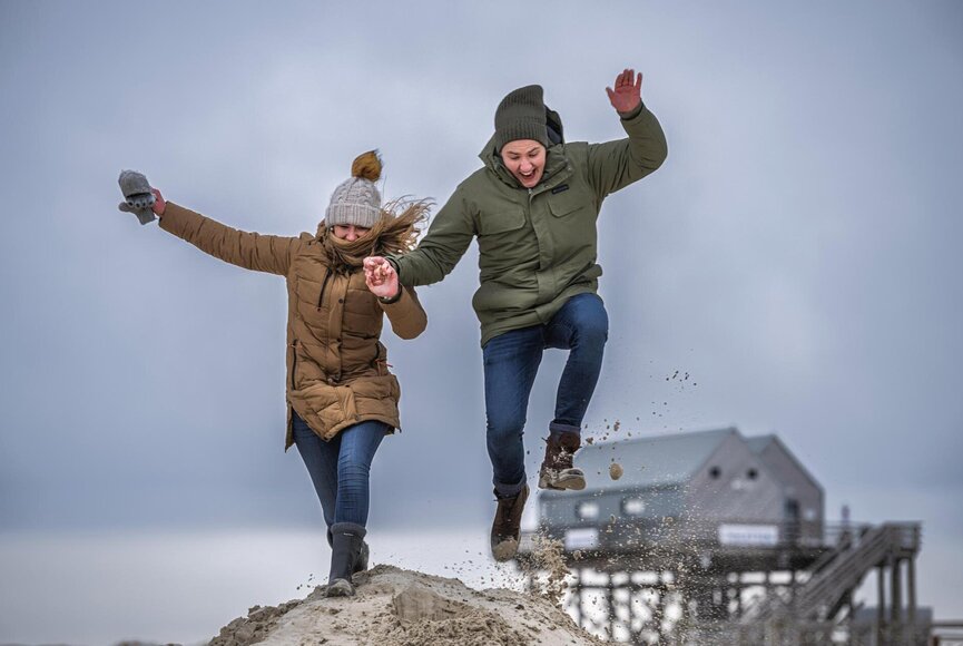 Pärchen tobt am Strand über einen Sandhügel