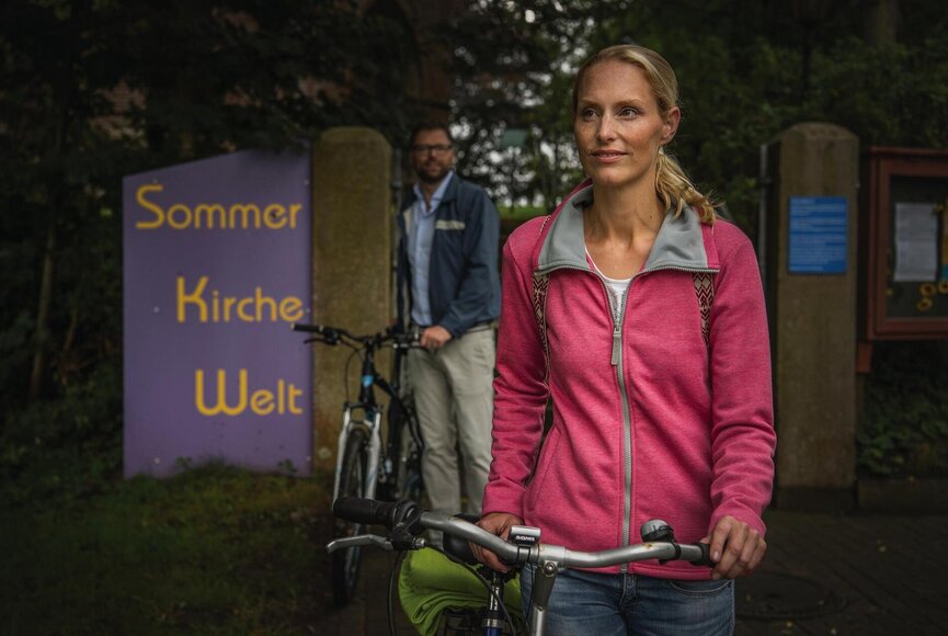 Paar bei der Ankunft der Kirche in Welt mit einem Schild der "Sommer Kirche Welt" im Hintergrund