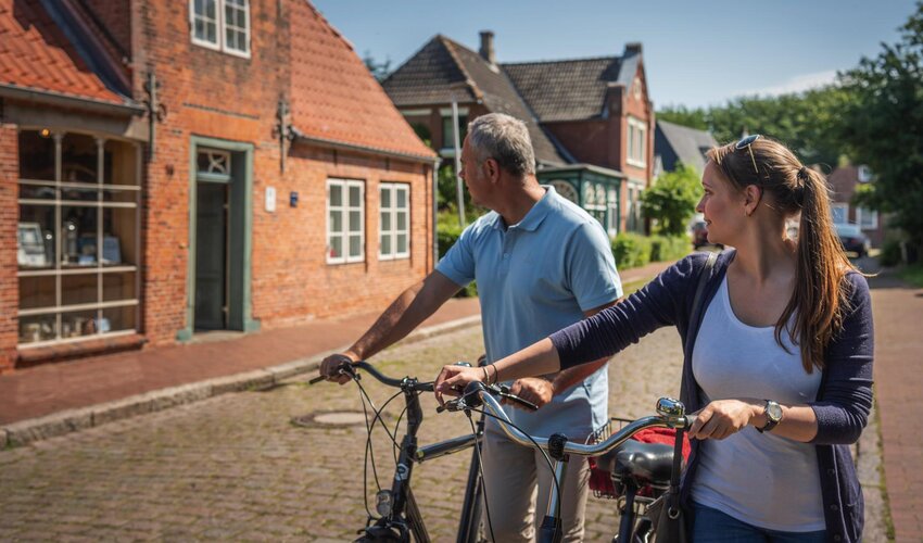 Paar mit Rädern im Dorfkern vor dem historischen Kaufmannsladen Haus Peters