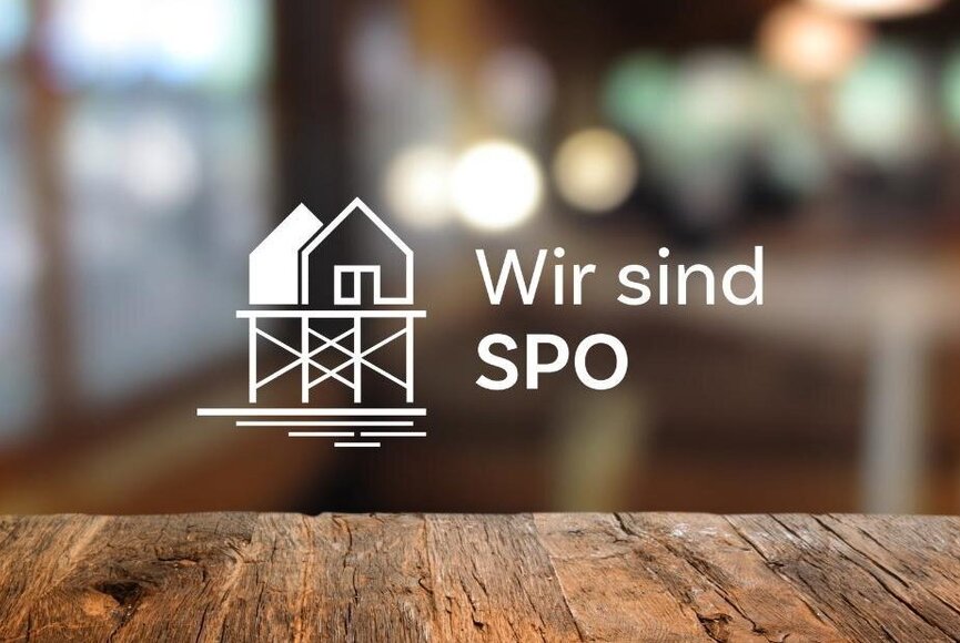 wirsindspo-logo-2023-website Logo der Partnermarke "Wir sind SPO" mit Pfahlbau vor verschwommenem Hintergrund