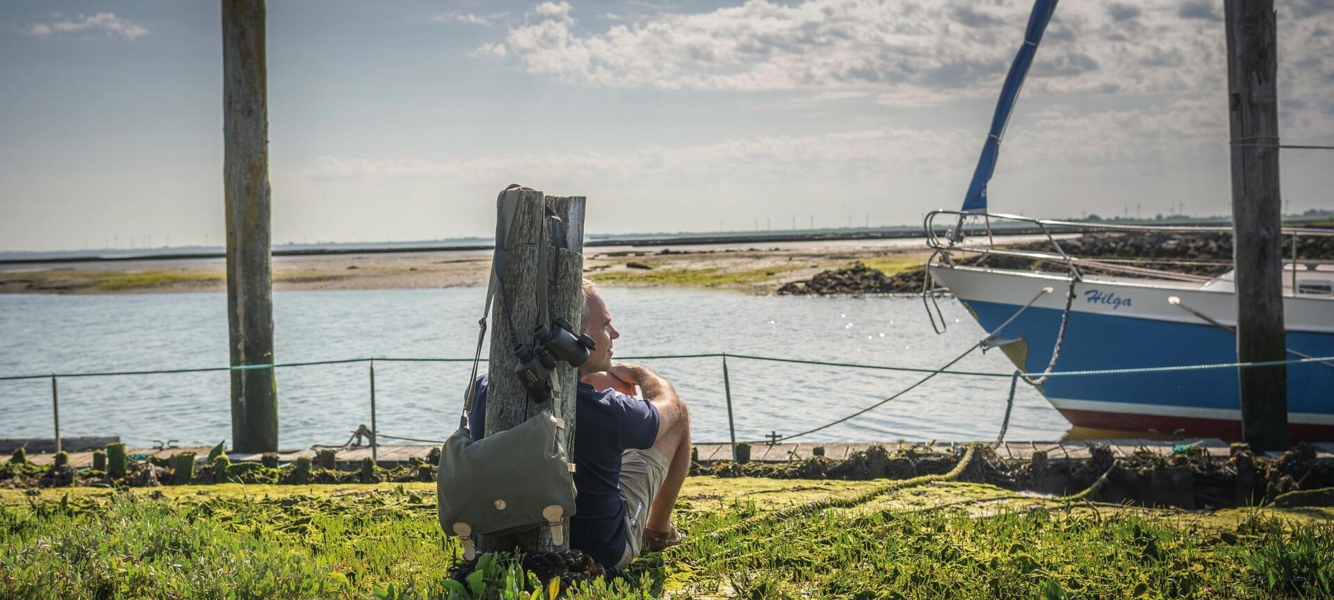 Mann lehnt an einen kleinen Pfahl und schaut auf das Wasser im Hafen vom Tetenbüllspieker