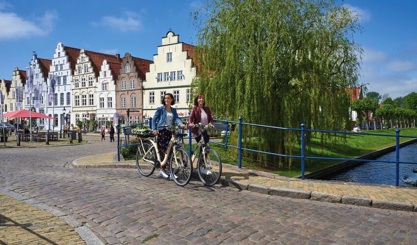 zwei Freundinnen mit dem Rad auf einer Grachtenbrücke