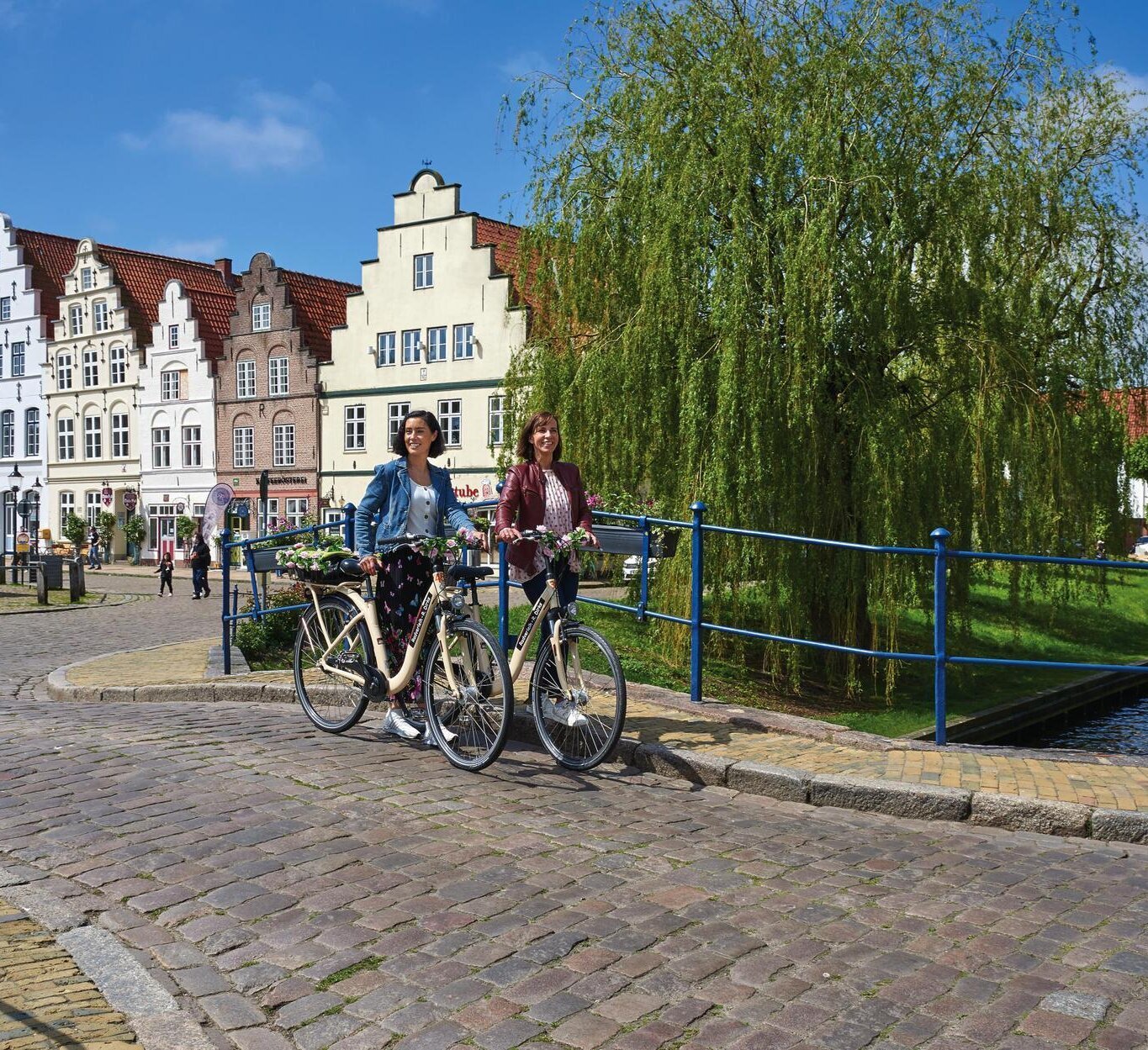 zwei Freundinnen mit dem Fahrrad auf einer Grachtenbrücke
