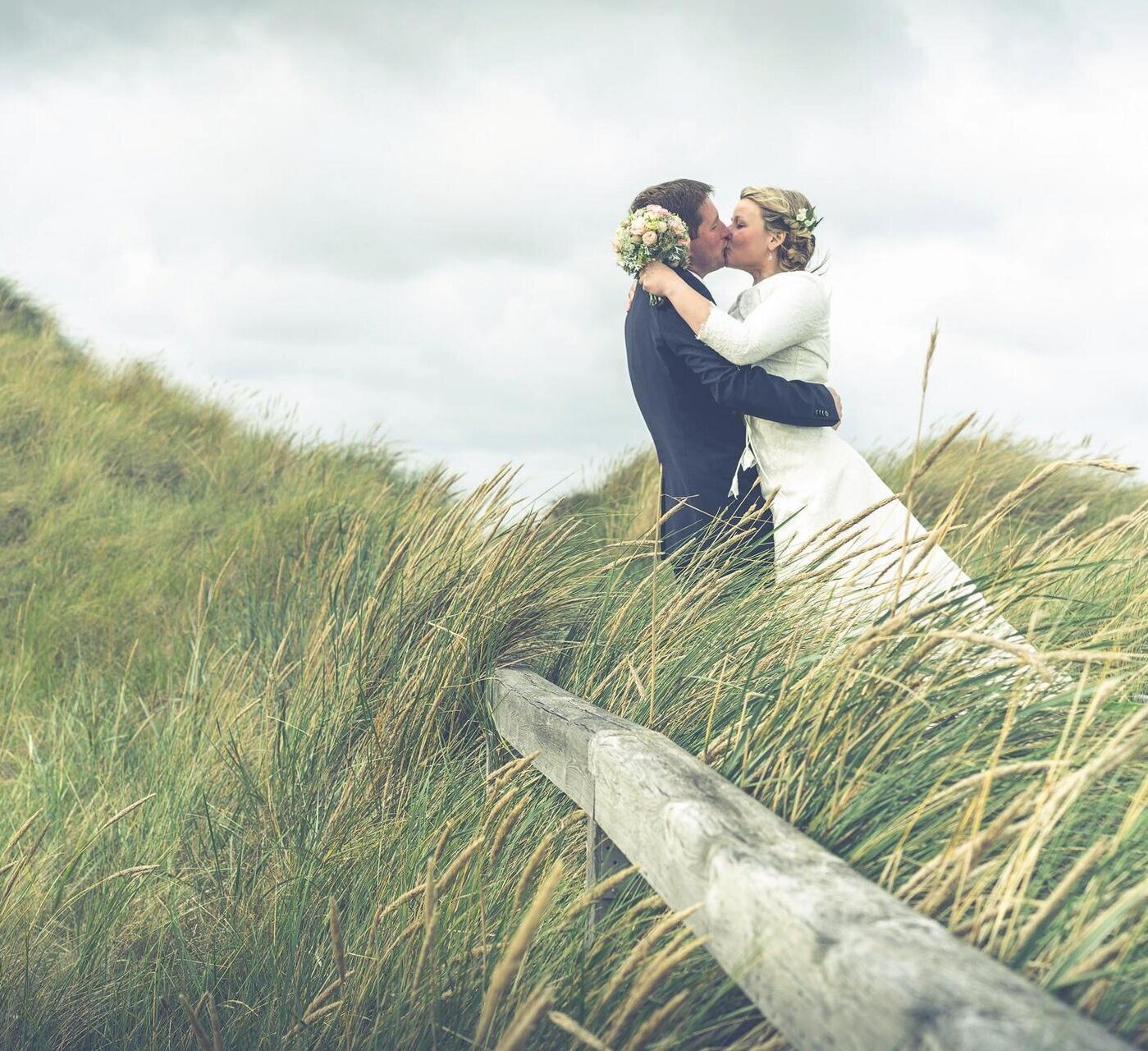 Hochzeitspaar küsst sich in der Dünenlandschaft