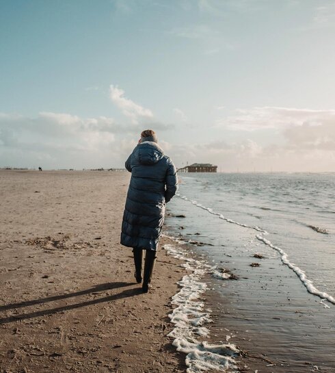 Frau bei herbstlichem Strandspaziergang an der Wasserkante