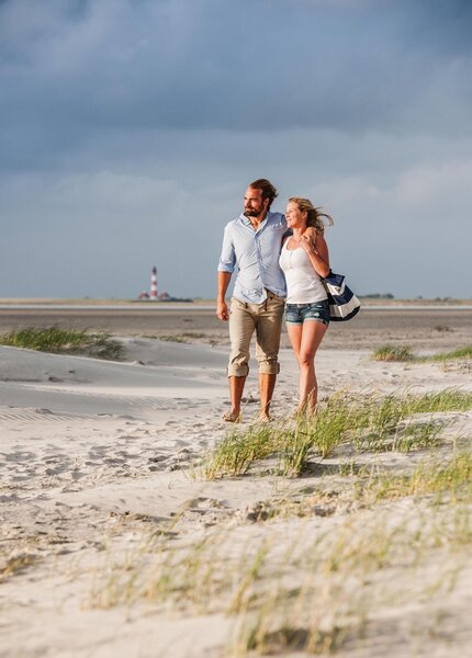 A couple taking a walk on the beach with the "Westerhever" lighthouse in the background